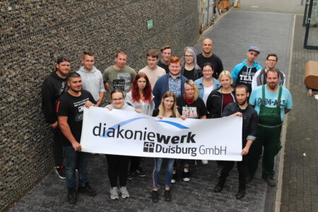 Eine große Gruppe von Menschen, die ein großes Plakat diakoniewerk Duisburg halten.