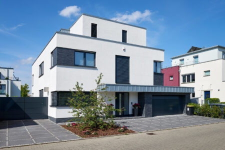 Ein modernes, zweistöckiges Wohnhaus mit weißer Fassade und schwarzen Akzenten. Das Haus hat große Fenster, eine Garage und einen gepflegten Vorgarten.