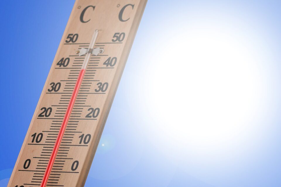 Holzthermometer in Celsius mit roter Flüssigkeitssäule knapp über 30 Grad vor blauem Himmel mit großer, greller Sonne.